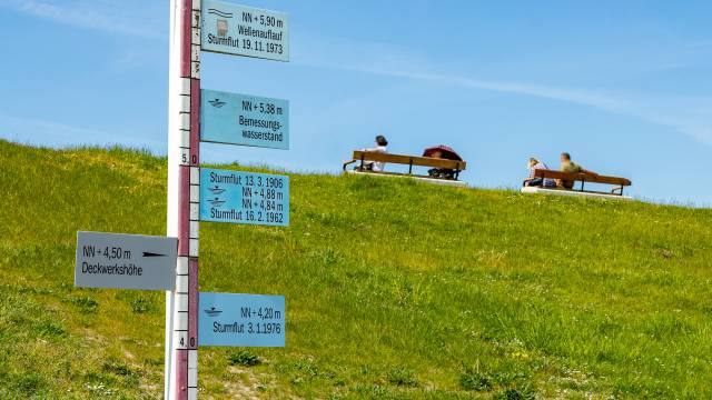 Schilder zur Deichsicherheit und man sieht Bänke mit Menschen