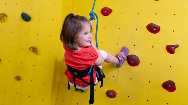 Mädchen hängt am Seil in der Kletterwand