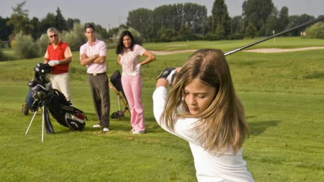 Mädchen spielt Golf und die Erwachsenen schauen zu