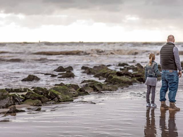 Papa und Tochter stehen an der Küste und schauen auf die Nordsee