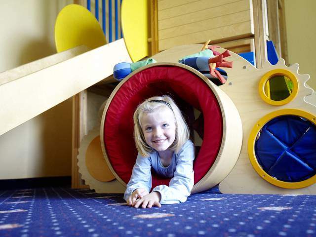 Mädchen schaut aus einer Röhre im Kinderspielbereich des Hotel Deichkrone