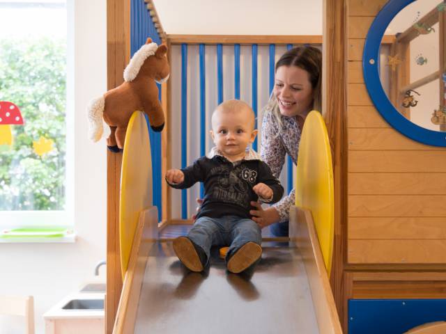 Kleiner Junge sitzt auf einer Kinder rutsche und die Mutter hält ihn 