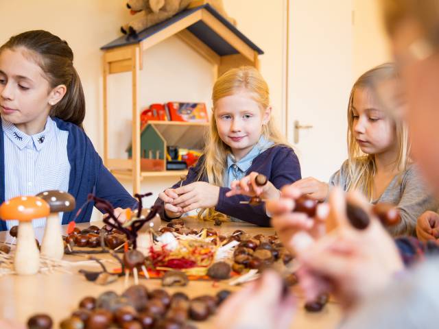 Mädchen sitzen am Tisch und basteln Herbstdeko