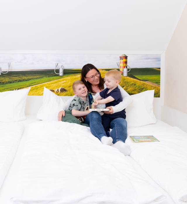 Mutter schaut mit ihren zwei Kindern ein Buch im Bett an