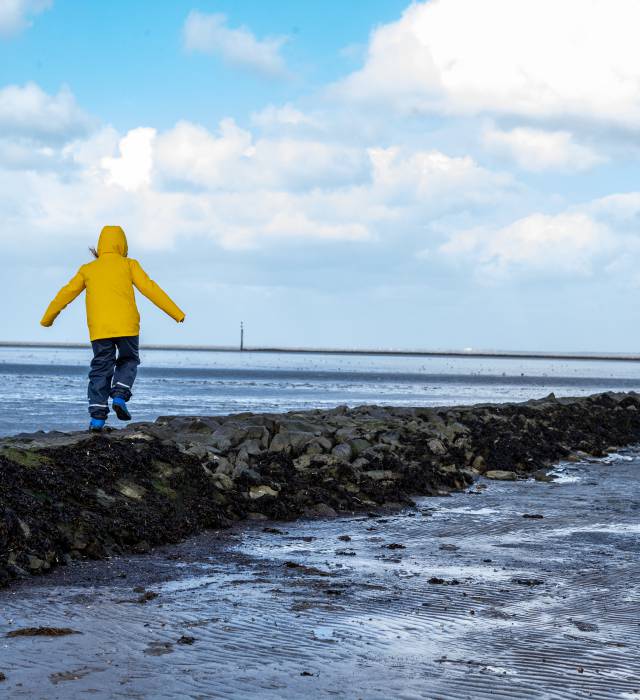 Kind mit gelber Jacke läuft über Steine an der Nordsee