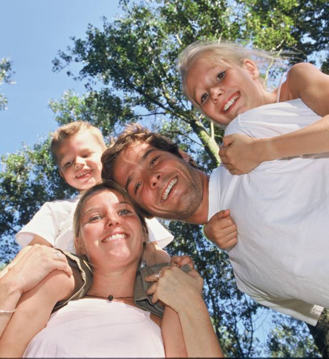 Mama und Papa haben Kinder auf dem Rücken und lachen in die Kamera