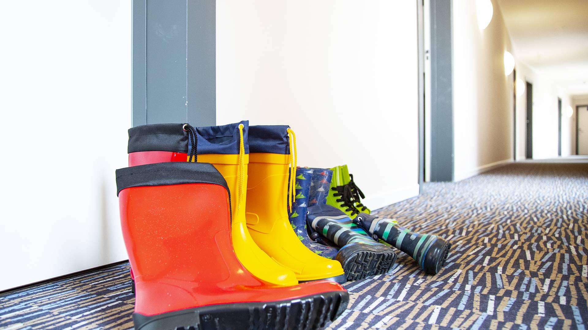 Verschiedene Gummistiefel stehen vor dem Hotelzimmer im Flur