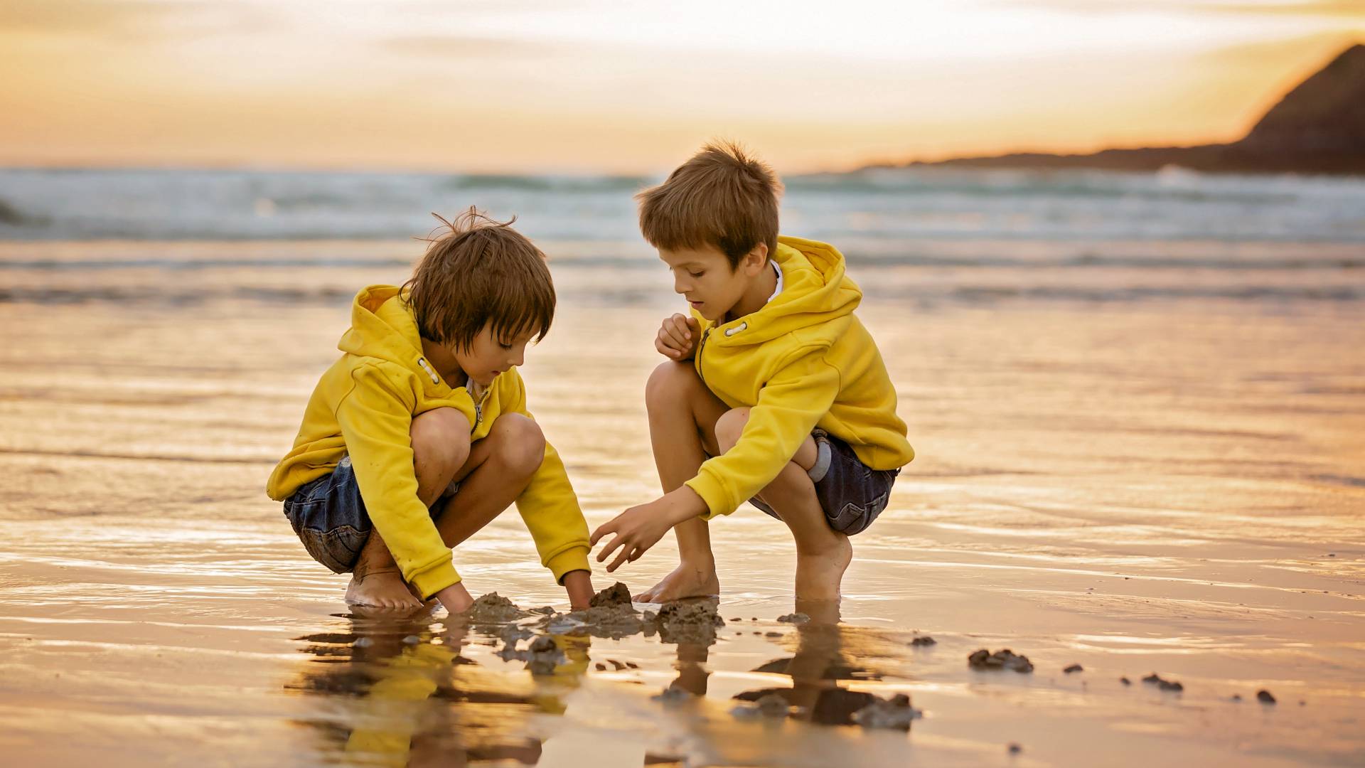 Zwei Jungs mit gelben Pullis spielen mit Sand bei Ebbe in der Nordsee