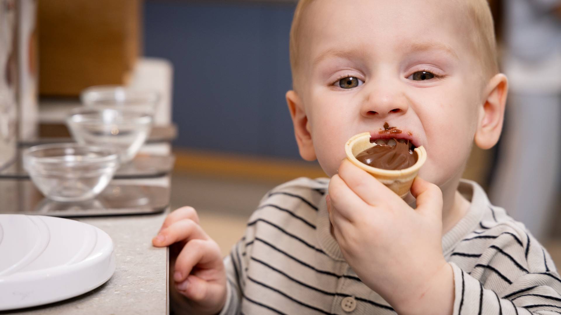 Kleiner Junge beißt in Nuss-Nougat-Creme am Frühstücksbuffet