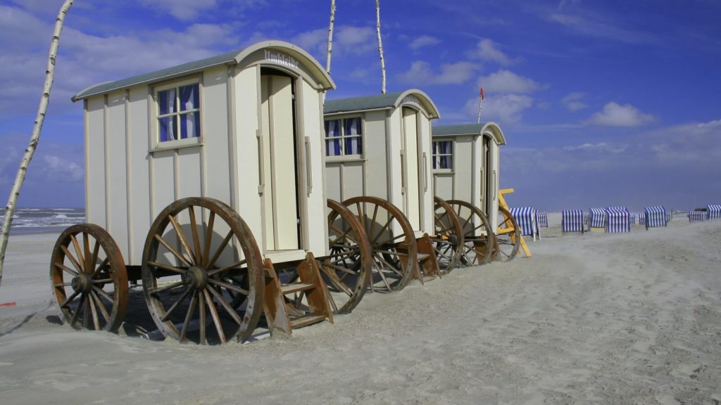 Drei weiße Holz-Zirkuswägen stehen auf dem Norderney Strand. Die Wagen wurde zu Umkleiden umgebaut.